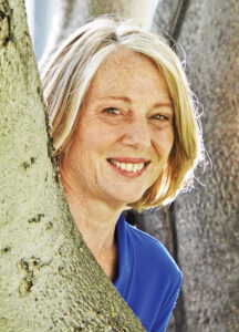 The photo of a woman smiling and peeking from behind a tree