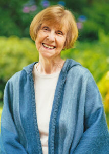 Picture of the author, an older white woman wearing a white sweater and blue jacket and smiling at the camera.